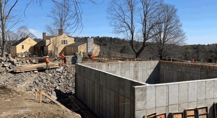 The dining commons concrete foundation will include a root cellar. The existing 18th century farmhouse (background) will be retrofitted in a later phase.